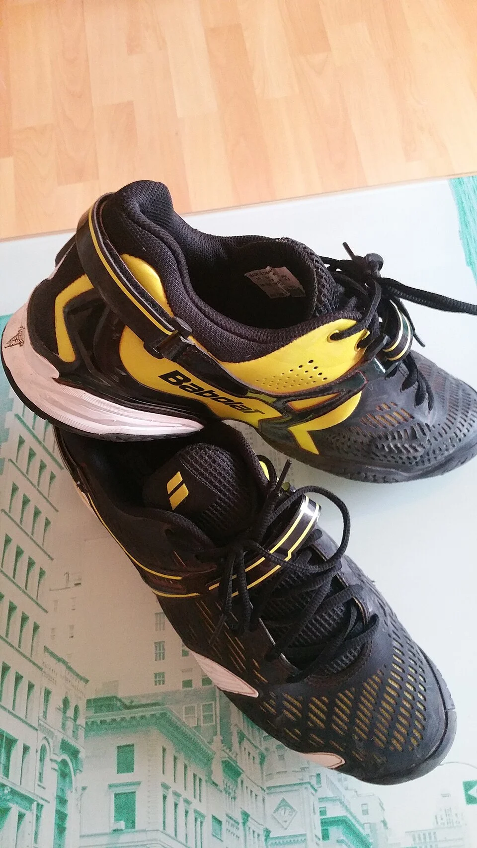 A pair of black and yellow Babolat tennis shoes viewed from above