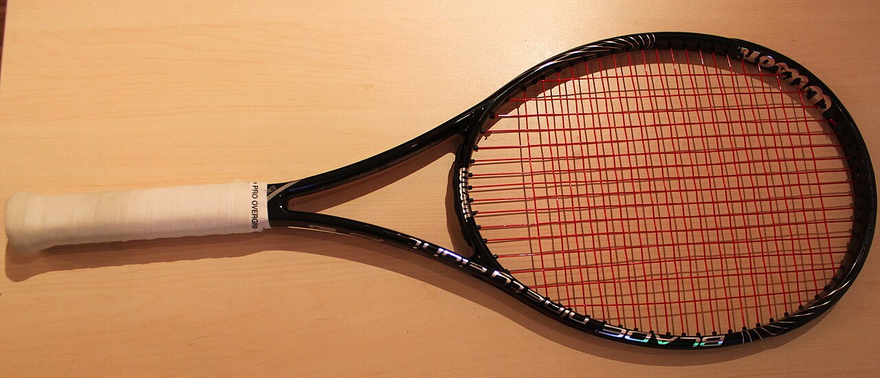 Ein früherer Wilson Blade 98 18×20 mit roten Saiten und weißem Griffband auf einer Holzfläche