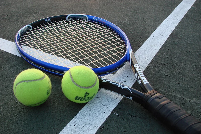 A tennis racquet and two balls resting on a court
