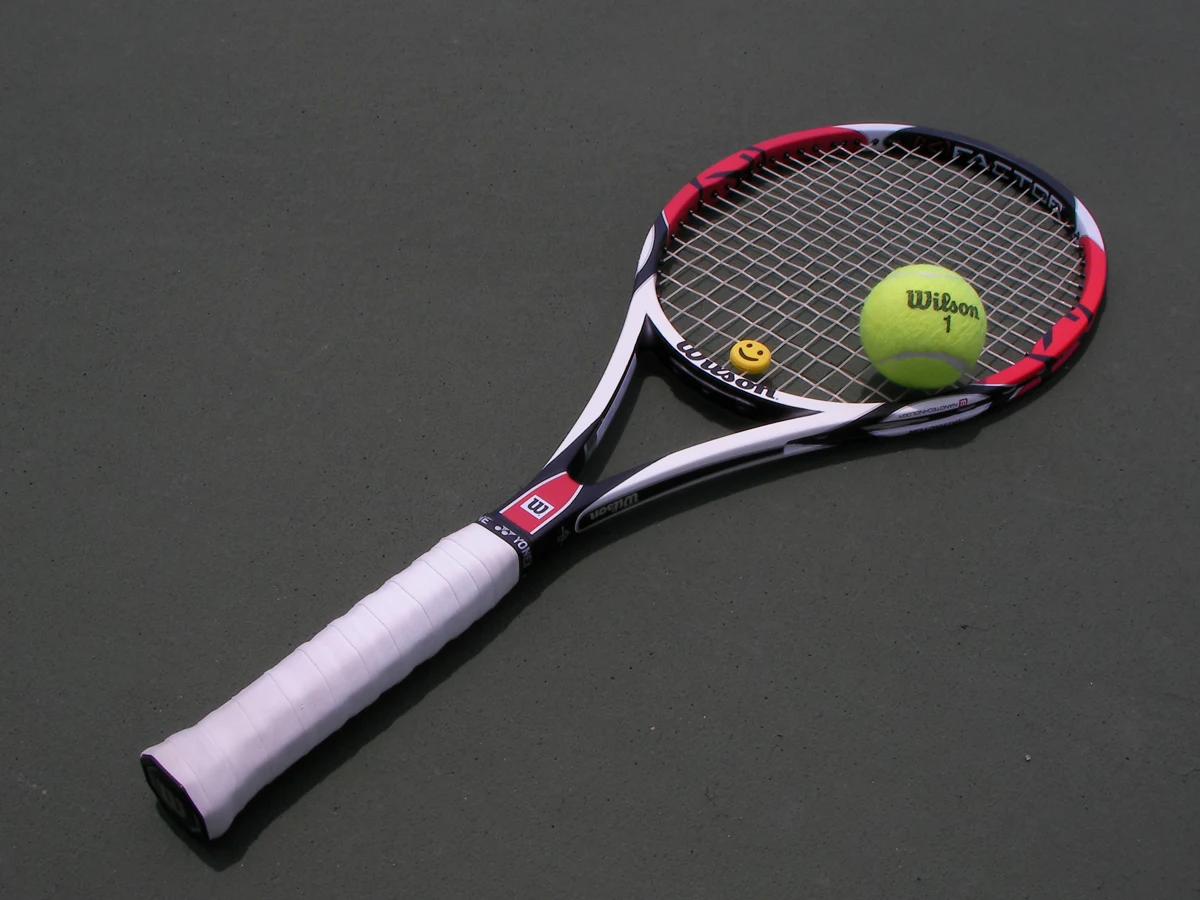 Ein Tennisschläger mit Ball auf dem Platz; Griff und Schlägerkopf sind sichtbar